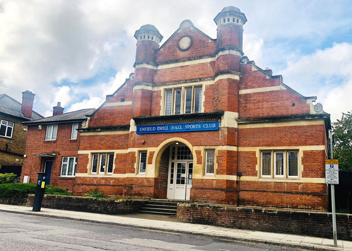 The red-brick front of Enfield Drill Hall Sports Club, with stone trim, an arched doorway and steps up to white double doors.