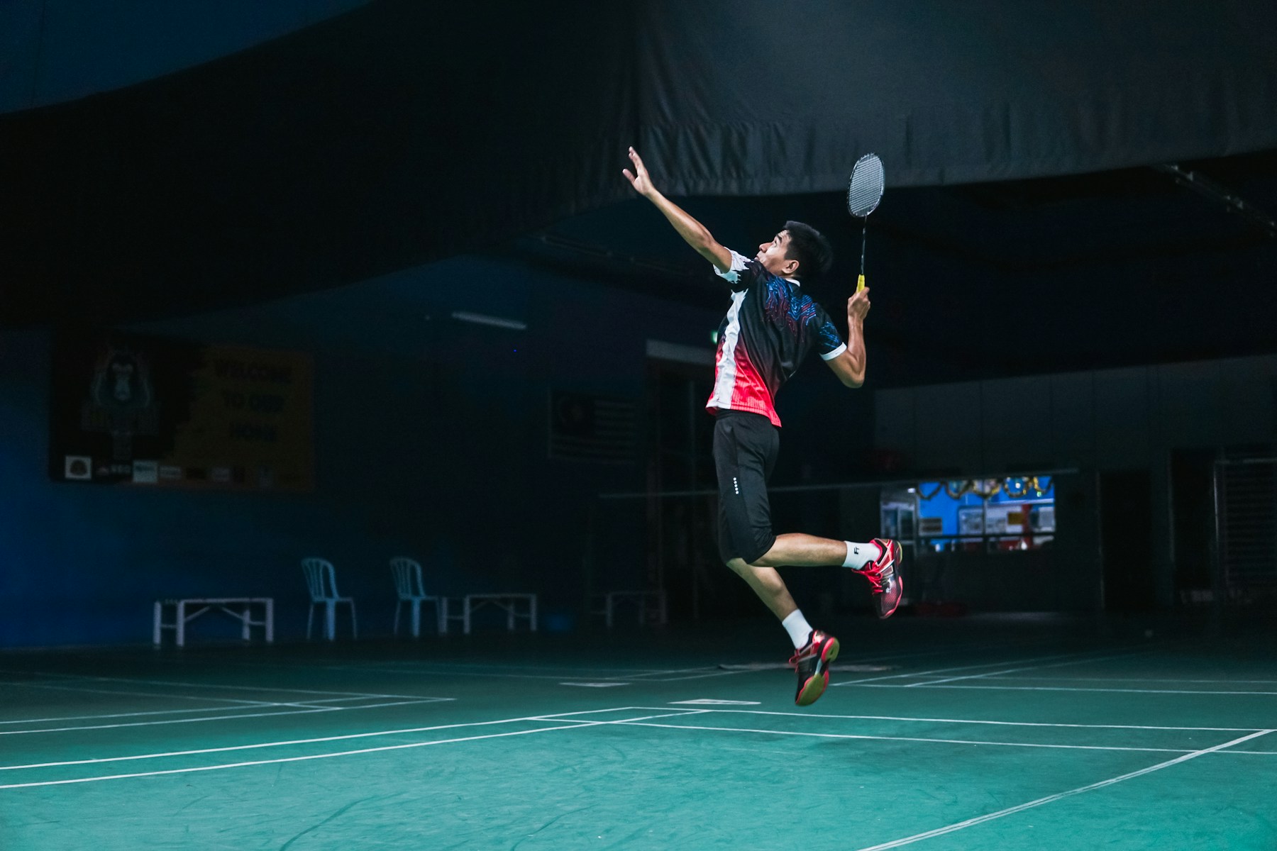A badminton player jumping to hit a shot on an indoor court.