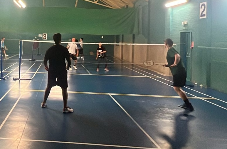 Players in a doubles rally on a blue court at the Drill Hall.