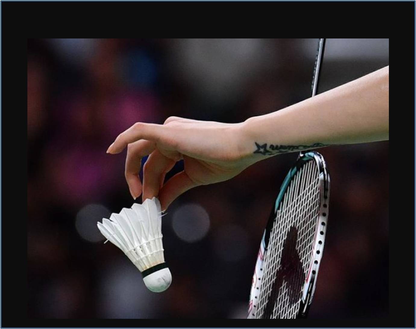 A hand holding a feather shuttlecock beside a badminton racket.